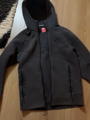 Nike tech  - Säljer en grå kofta från nike med dragkedja framtill och huva. Koftan har inga fel och den är i bra skick. 