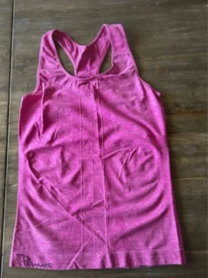 Rosa linnetopp från Panos Emporio - Säljer en sportig rosa linnetopp från Panos Emporio med racerback och diskret mönstrad struktur i tyget. Toppen är ärmlös och har en tight passform, perfekt för träning eller aktiva dagar. Logga finns tryckt nertill på framsidan och baksidan. Storlek XS/S