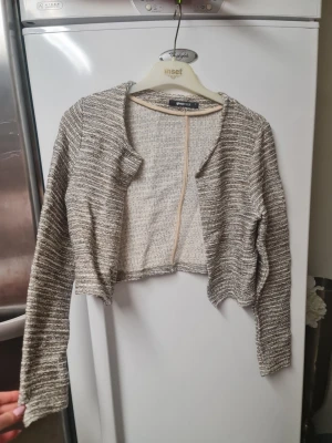 Randig croppad kofta från Gina Tricot - Säljer en croppad kofta från Gina Tricot i storlek S. Koftan är randig i beige och grå toner, har lång ärm och är tillverkad i ett stickat material. Perfekt att slänga över en topp för en chill look. Snyggt avslut nertill och öppen framtill.