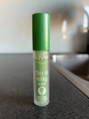 NYX This Is Milky Gloss Mint Choc - NYX Professional Makeup This Is Milky Gloss i färgen Mint Choc Chip Shake är ett läppglans med mjölkig grön ton och mintchokladsmak. Kommer i en smidig tub med grön kork och transparent plastförpackning. Perfekt för dig som gillar gloss med lite extra twist och kul färg. Oanvänd 