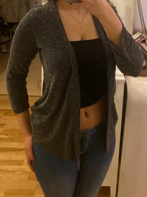 Glittrig svart kofta från Capuccini strl S - Snygg svart/ silvrig glittrig kofta från Capuccini i storlek S med glittriga inslag. Koftan har öppen front och trekvartsärma. 