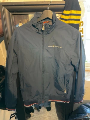 Mörkblå vindjacka från Sail Racing - Snygg mörkblå vindjacka från Sail Racing med dragkedja framtill och två sidofickor med zip. Jättebra skick, storlek S