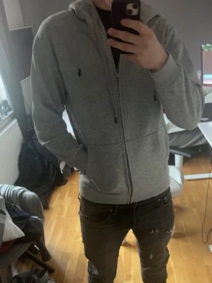 Grå hoodie från Polo Ralph Lauren - Snygg grå hoodie från Polo Ralph Lauren med dragkedja och luva. Använts 2-3 gånger nästan helt ny .