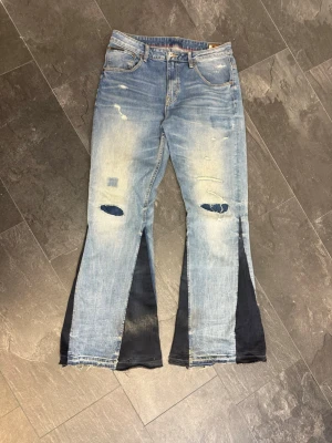 1 OF 1 MARES TAKEOVER ”BLUE” FLARED JEANS - Bootcut jeans från Levi's i ljusblå tvätt med slitna detaljer och hål på knäna. Byxbenen har svarta kontrastpaneler och råa, fransiga kanter längst ner. Klassisk femficksmodell med knapp och dragkedja. Perfekt för dig som gillar en edgy och unik stil.