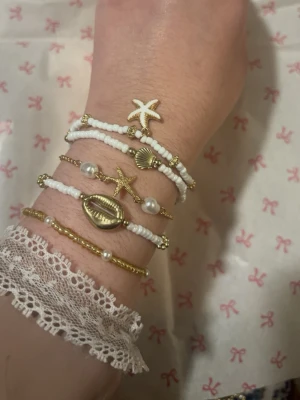 Handgjorda armband  - Armband med vita och guldfärgade pärlor, dekorerad med snäckor, sjöstjärnor och små gulddetaljer. 