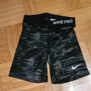 Nike Pro svarta träningstights shorts XS - Nike Pro shorts i svart med grått mönster och bred resår i midjan med logga. Tight passform och tillverkade i stretchigt syntetmaterial, perfekta för träning eller sport. Snyggt vågigt mönster som ger en cool look.