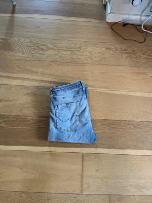 Slim fit jeans från Jack & Jones - Snygga ljusgrå slim fit jeans från Jack & Jones, modell Glenn. Klassisk femficksdesign med knapp och dragkedja i midjan. Jeansen är tillverkade i bomull och har en smal passform som sitter snyggt längs benen. Perfekt för dig som gillar en modern och stilren look. Byxorna är använda få gånger och har inga skador