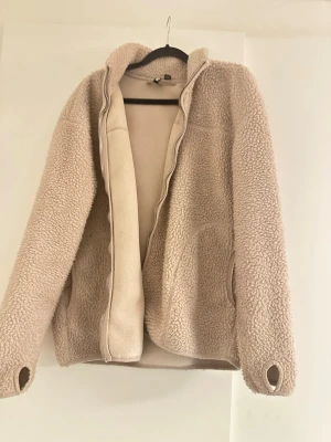 Beige teddyjacka från Pieces - Mysig beige teddyjacka från Pieces med dragkedja och praktiska fickor. Jackan har långärmade ärmar med tumhål och är tillverkad i fluffigt syntetmaterial som ger en chill vibe. Perfekt för lager-på-lager under höst och vinter.
