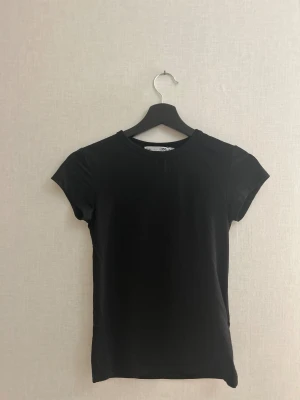 Svart t-shirt från 157, storlek M - Säljer en fin mjuk stilren t-shirt från Lager 157 i storlek M! Matrialet innehåller 90% polyamid och 10% elastan, vilket ger en skön och stretchig passform. Perfekt som basplagg i garderoben eller för träning. Själv använt den som en helt vanlig T-shirt och stylat upp den med smycken och ett par lågmidjade jeans 🥰Har kommit till användning väldigt få gånger och är i mycket bra skick!! Djur och rökfritt hem! ❤️ Pris kan diskuteras!
