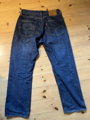 Levi's Premium blå jeans W32 L30 - Snygga Levi's Premium jeans i klassisk blå denim med raka ben och normal passform. Jeansen har fem fickor, kontrastsömmar och ikonisk läderpatch bak i midjan. Perfekta för dig som gillar tidlös stil och kvalitetskänsla. De är använda i ungefär 1 och en halv vecka och är i en extremt fet mörkblå färg! Hör av dig vid frågor🙏