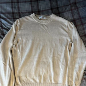 Les deux - Snygg beige stickad tröja från Lads Dept med rund hals och ribbade muddar vid ärmslut och nederkant. Perfekt för dig som gillar enkel och stilren design. Långärmad modell som passar till många olika outfits.