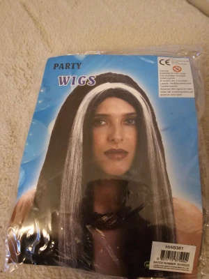Svart och orange peruk med syntethår - Cool peruk i svart och orange syntethår, perfekt för att sticka ut på maskerad eller temafest. Långt hår med tydliga färgblock som ger en riktigt edgy look. Sitter bekvämt på huvudet och är lätt att styla för en unik stil.