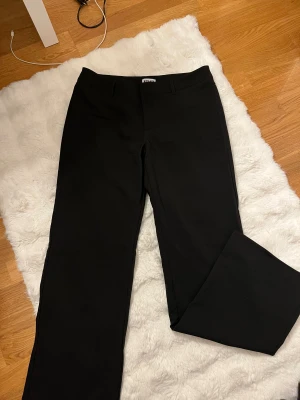 Svarta kostymbyxor från Madlady - Svarta kostymbyxor från Madlady i modellen Tall, med klassisk rak passform och diskreta fickor bak. Byxorna har hällor för bälte och är gjorda i ett mjukt material som sitter snyggt. Perfekta för dig som gillar stilrena och enkla plagg. Inte använt en endaste gång 