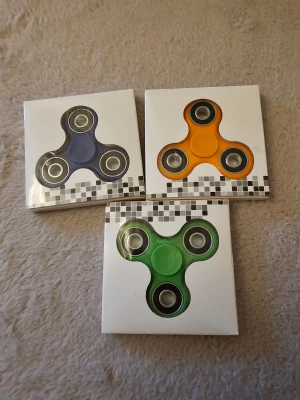 3 Hand Spinners - Blå, Orange, Grön - Tre handspinners i olika färger: blå, orange och grön. Perfekt för både arbete, skola och hemma.