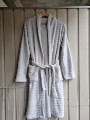 Vit fluffig morgonrock - Supermjuk och fluffig vit morgonrock. Är fortfarande i gott skick förutom att några styng på ena enden av snöret som har gått upp, se bild. Säljer pga att den inte kommer till användning längre.