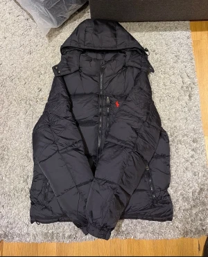 Polo Ralph Lauren jacka - Säljer en svart pufferjacka från Polo Ralph Lauren med huva och dragkedja framtill.  