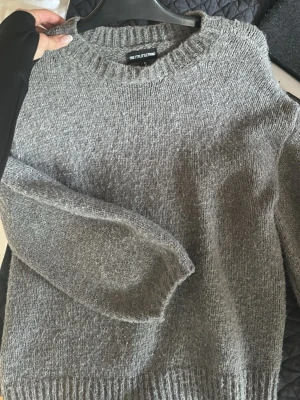 Grå stickad tröja PrettyLittleThing - Mysig grå stickad tröja från PrettyLittleThing i storlek S. Tröjan har rund hals, ribbade muddar och lång ärm. Perfekt för kyliga dagar och enkel att matcha med jeans eller leggings. Den har en loose passform och är superbekväm.