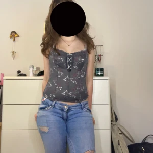 Blommig korsettopp från Triumph - Supersnygg mörkgrå korsettopp från Triumph med blommigt mönster i vinrött och vitt. Toppen har snörning framtill och cropped passform. Materialet är meshigt och lätt, samt väldigt stretchigt. ❤️❤️