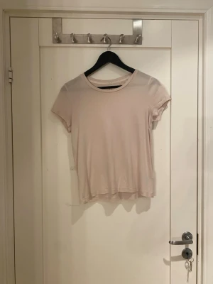 Ljusbeige t-shirt från Lindex - En enkel och mjuk ljusbeige t-shirt från Lindex i storlek S. T-shirten har rund hals och korta ärmar, perfekt för en chill och avslappnad stil. Materialet känns lätt och skönt mot huden, och den neutrala färgen gör den enkel att matcha med allt.