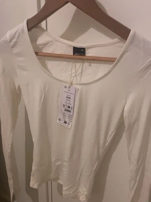 Vit långärmad topp från Gina Tricot - Säljer en helt ny enkel långärmad topp från Gina Tricot. Har även utsvängda ärmar.