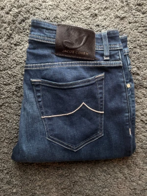 Jacob Cohën Style 688 (Bard) - Otroligt feta Jacob Cohen jeans. Nytt skick. Sällsynta kontrastsydda detaljer, unika vita dekorationssömmar på bakfickorna samt patch i mörkt skinn. Silverfärgade knappar och rutigt tyg på insidan. 📏 Mått: Innerben 80 cm, midja 46 cm, ytterben 104 cm 📐 Passform: Rak 🎅 Modell: Personen på bilden är 187 cm ✅ Skick: 10/10, helt nya, använda 2 gånger 🧵 Modell: J688 COMF (Bard) 🧩 Material: Premium denim 🇯🇵🇮🇹 ✨ Otroligt snygga och stilrena jeans med unika detaljer ‼️Skickas samma dag eller dagen efter‼️