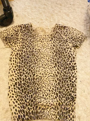 Leopardmönstrad stickad topp - Säljer en kortärmad topp med leopardmönster i beige och bruna toner. Toppen är stickad och har rund hals, ribbad nederkant och ärmar. Perfekt för dig som gillar djurmönster och vill sticka ut lite extra.