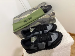 Valentino Rockrunner sneakers svart/grå - Säljer ett par Valentino Rockrunner sneakers i svart och grått med snyggt kamouflagemönster. Skorna har snörning, rund tå och platt sula. Ovandelen är i mesh och mocka med detaljer i skinn. Kommer med originalkartong och grön dustbag. ( finns två par) 