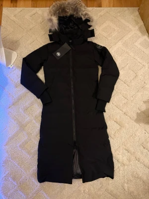 Canada Goose Black Label Mystique Parka – Svart - Canada Goose Black Label Mystique Parka – Svart 🧥 Modell: Mystique Parka – lång, varm och exklusiv 🎯 Label: Black Label (diskret logga i ton-i-ton) 👤 Storlek: S 🖤 Färg: Svart ✨ Skick: 10/10 – helt ny, aldrig använd 🏷️ Detalj: Tag kvar 💎 Märke: Canada Goose