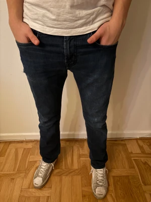 Tramarossa Jeans - Säljer ett par mörkblå jeans från Tramarossa med snygga röda sömmar på bakfickorna och en cool läderpatch med logga. Jeansen har klassisk femficksdesign, raka ben och normal passform. Materialet är slitstarkt jeans och detaljerna ger en unik vibe.