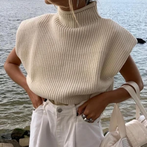 Beige stickad polotröja från Zara - Säljer en beige stickad polotröja från Zara. Tröjan är ärmlös med hög krage och har en chunky ribbstickad struktur. Passformen är loose och den är riktigt mjuk och skön.
