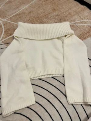 Vit croppad off shoulder tröja  - Säljer en vit croppad off shoulder tröja med långa ärmar. Tröjan är stickad och har ribbade muddar vid ärmslut och nederkant. Perfekt för att skapa en cool lager-på-lager look under hösten och vintern.