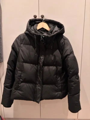 Svart pufferjacka från ONLY - Svart pufferjacka från ONLY med huva och snörning. Jackan har quiltad design, dragkedja framtill och praktiska fickor på sidorna. Perfekt för kalla dagar och har en loose passform som ger en chill vibe. Endast använd en halv säsong och är i jättebra skick. Nypris 1100kr