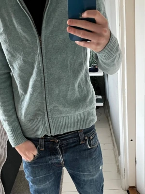 Gråblå kofta från WoolOvers med dragkedja - Säljer en gråblå kofta från WoolOvers i storlek M. Koftan har ribbad krage, muddar och nederkant samt en hel dragkedja framtill. Materialet är mjuk ull och passformen är normal. Perfekt för kyliga dagar och enkel att matcha med jeans eller chinos. Skulle säga att den passar S/M eller S i storleken, hör av er vid funderingar😁