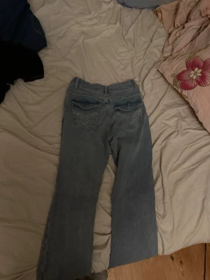 Blå jeans med broderade bakfickor - Snygga ljusblå jeans med but cut och broderade detaljer på bakfickorna. Jeansen har klassisk femficksdesign och är tillverkade i jeansmaterial. Nedtill på benen finns slitningar då jag har gått på dom annars mycket bra skick 