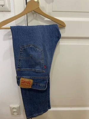 Levi's 505 blå jeans - Klassiska blå Levi's 505 jeans med rak passform och ikonisk läderpatch bak. Jeansen har fem fickor, normal midja och är tillverkade i slitstarkt denim. Perfekta för dig som gillar tidlös stil och vill ha ett par riktigt schyssta jeans. 