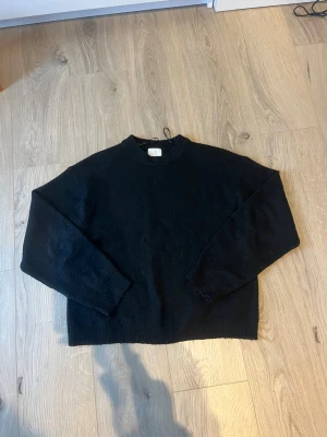 Svart stickad tröja från H&M XS - En enkel svart stickad tröja från H&M i storlek XS. Tröjan har rund hals, långa ärmar och ribbade muddar vid ärmslut och nederkant. Perfekt att slänga på sig när det är kyligt ute och passar till många olika stilar.
