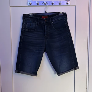 Mörkblå jeansshorts Jack & Jones - Snygga mörkblå jeansshorts från Jack & Jones i loose fit. Klassisk femficksmodell med uppvikta benslut och midwaist. Perfekta för sommaren när du vill ha en avslappnad och cool stil.