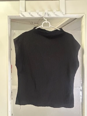 Svart ribbad ärmlös topp - Svart ribbad topp med ärmlös design och rund hals. Materialet är stickat och har en mjuk känsla. Passformen är normal och toppen har en enkel, stilren look som funkar till många olika outfits.