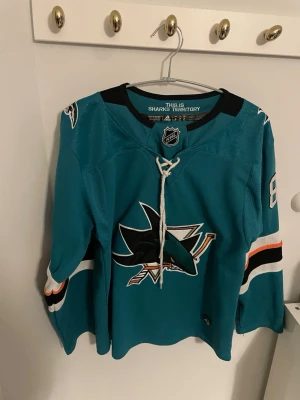 San Jose Sharks hockey tröja - Bilderna visar en San Jose Sharks hockeytröja från Adidas med namn och nummer Burns 88, men ingen sko finns med.