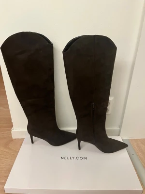 Bruna höga stövlar med klack från NAKD - Säljer ett par bruna höga stövlar från Lojsans kollektion med NAKD med spetsig tå och smal klack. Stövlarna är tillverkade i mocka och har dragkedja på insidan. Endast använda 1 gång så väldigt bra skick