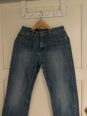 Blå lågmidjade jeans med zigzag-detaljer från kaiweizhi - Säljer ett par blå jeans från Kavenzi med snygga zigzag-broderier på bakfickorna. Jeansen har klassisk femficksdesign, normal passform och raka ben. Materialet är slitstarkt denim i bomull och färgen är en tvättad blå ton.