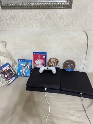 Två stycken PlayStation 4 (en slim)+ spel och handkontroll - Två PlayStation 4-konsoler med en vit DualShock 4-handkontroll. Flera populära spel ingår: FIFA 19, FIFA 20, FIFA 21, Uncharted 4 och GTA V. Konsoler och tillbehör ser ut att vara i gott skick.