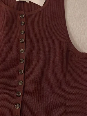 Vinröd ribbad linnetopp med knappar - Säljer en vinröd linnetopp från ZARA med ribbad struktur och snygga knappar framtill. Toppen är ärmlös och har rund halsringning. Materialet känns mjukt och stretchigt, perfekt för att styla med jeans eller kjol.