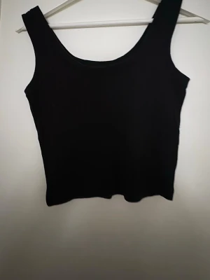 Svart ribbad linnetopp - Säljer en svart ribbad linnetopp med breda axelband och rundad halsringning. Toppen är ärmlös och har en enkel, stilren design som funkar till många olika looks. Materialet känns mjukt och stretchigt, perfekt för varmare dagar.