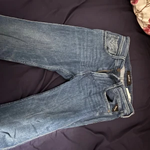 Replay Anbass blå jeans - De är 28/30 kan sitta som 29/30 ungefär. Snygga blå jeans från Replay, modell Anbass. Klassisk femficksdesign med dragkedja och knapp framtill. Jeansen har en rak passform och diskreta detaljer på bakfickorna. Tillverkade i slitstarkt jeansmaterial som är bekvämt och följsamt.