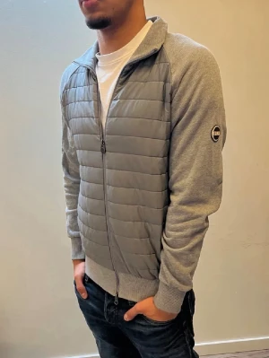 Grå cardigan jacka från Colmar - Snygg grå jacka från Colmar med quiltad front och rygg, samt mjuka ärmar och sidor i sweatshirtmaterial. Jackan har hel dragkedja och ribbade muddar. Perfekt för dig som gillar en clean och sportig look. NYPRIS:3999Kr, Mitt pris:1399Kr ✅