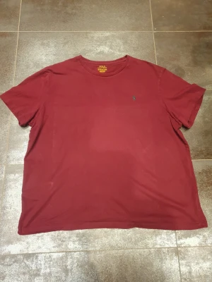 Vinröd t-shirt från Polo Ralph Lauren - Säljer en vinröd t-shirt från Polo Ralph Lauren i storlek XXL. Klassisk rund hals och korta ärmar, med den ikoniska lilla logon broderad på bröstet. Tillverkad i mjuk bomull som är skön mot huden. Perfekt för dig som gillar stilrena och enkla plagg.