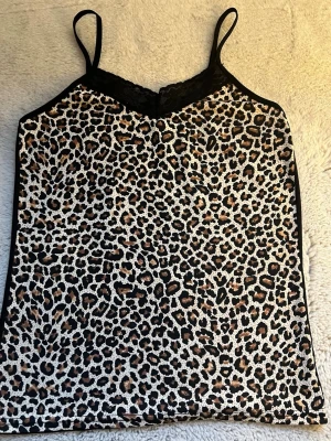 Leopardmönstrad linnetopp med spets - Säljer en snygg linnetopp med leopardmönster på framsidan och svart baksida. Toppen har tunna axelband och spetsdetalj vid halsringningen. Materialet känns mjukt och lätt, perfekt för varma dagar eller att styla lager på lager.Det finns också matchande trosor till denna fina linne i min profil!