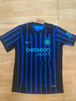 Inter Milan fotbollströja M - Snygg Inter Milan fotbollströja Nike i svart och blått med vertikala ränder. Tröjan har klubbmärke, sponsortryck och Nike-logga på bröstet. Tillverkad i lätt polyester med korta ärmar och rund hals. Perfekt för dig som älskar fotboll och vill ha en autentisk look. OBS: Tröjan är ej autentisk!