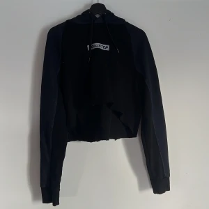 Svart croppad hoodie från Hollister - Svart hoodie från Hollister i storlek XL med croppad och rå kant nedtill.  Hoodien har snörning i luvan och ett broderat Hollister-märke på bröstet.  Tillverkad i mjuk bomull med fleece på insidan för extra komfort. Jag har själv klippt och färgat denna tröja. 